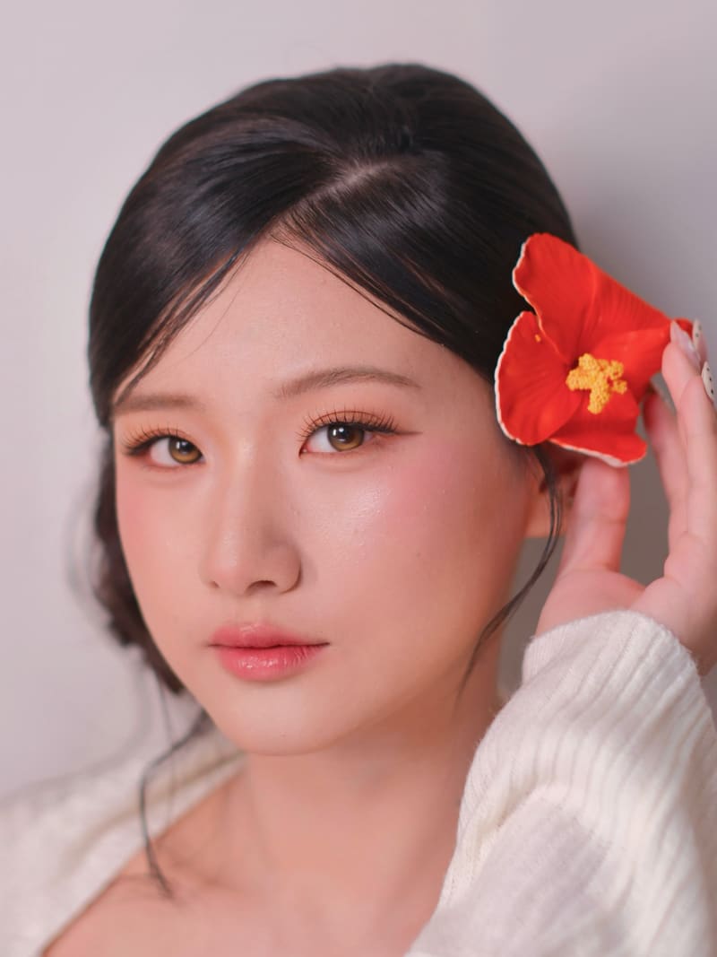 Woman holding a red hibiscus beside a soft low bun