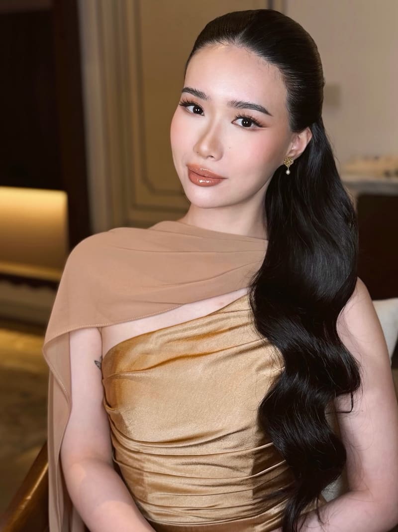 Woman in a gold dress with a long wavy ponytail over one shoulder