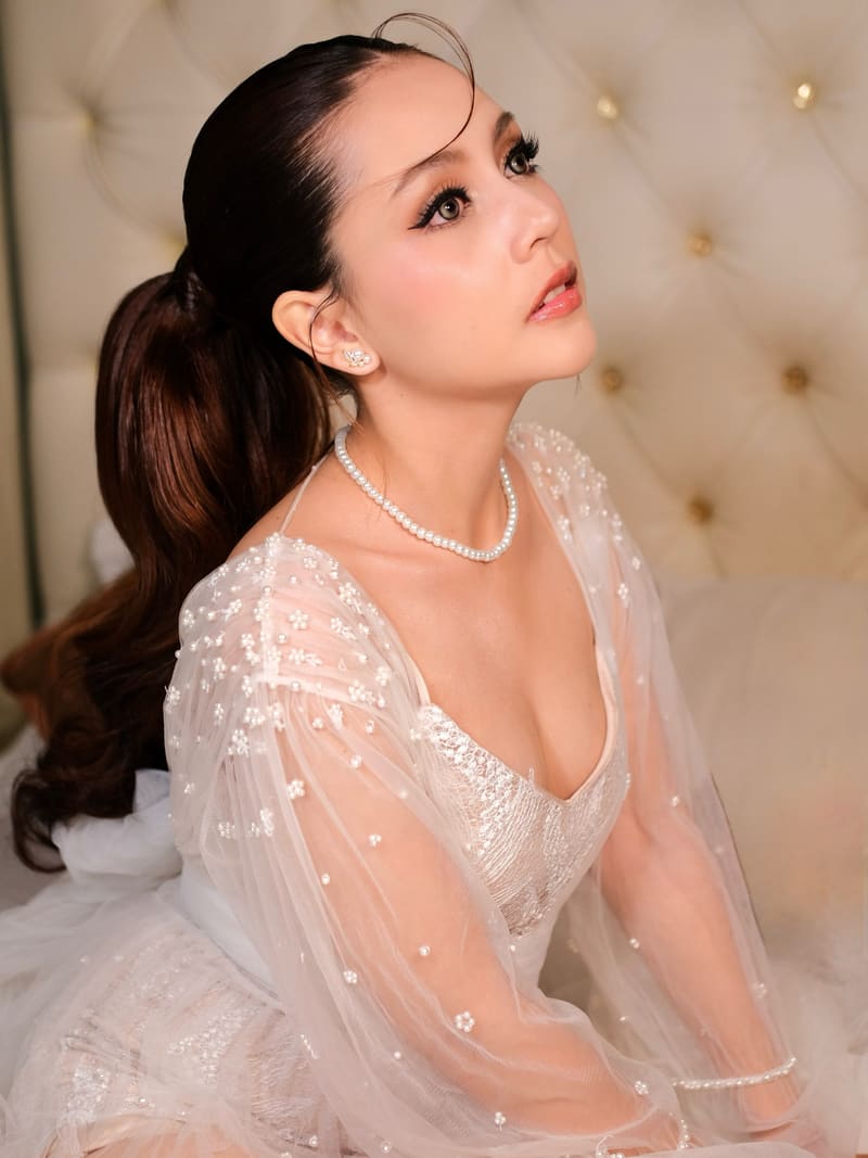 Woman in a sheer floral gown with a high wavy ponytail and pearls